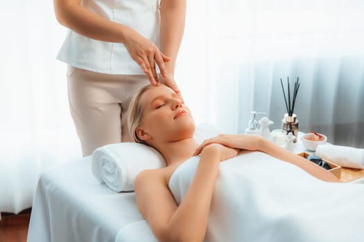 Caucasian woman enjoying relaxing anti-stress head massage and pampering facial beauty skin recreation leisure in dayspa modern light ambient at luxury resort or hotel spa salon. Quiescent