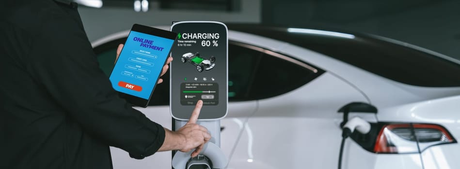 Young man travel with EV electric car to shopping center parking lot charging in downtown city showing urban sustainability lifestyle by green clean rechargeable energy of electric vehicle innards