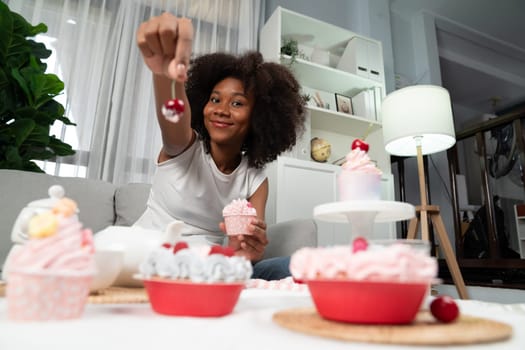 Beautiful young African blogger presenting piece of cupcake in concept showing special cuisine in pastel color. Content creating of social media with favorite sweets bakery dish. Tastemaker.