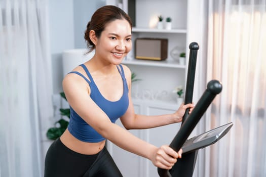 Energetic and strong athletic asian woman running on elliptical running machine at home. Pursuit of fit physique and commitment to healthy lifestyle with home workout and training. Vigorous