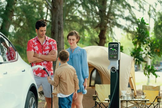 Outdoor adventure and family vacation camping in nature travel by eco friendly car for sustainable future. Lovely family recharge EV car with EV charging station in campsite. Perpetual