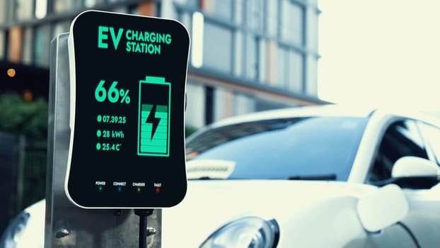 EV charging station display battery status interface for electric car, exemplifying green city with clean energy. Technological advancement of alternative energy sustainability utilization. Peruse
