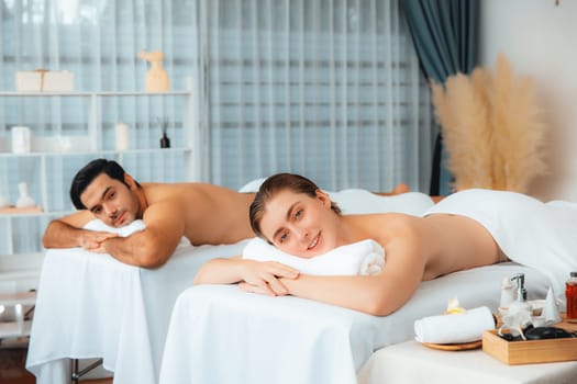 Caucasian couple customer enjoying relaxing anti-stress spa massage and pampering with beauty skin recreation leisure in day light ambient salon spa at luxury resort or hotel. Quiescent