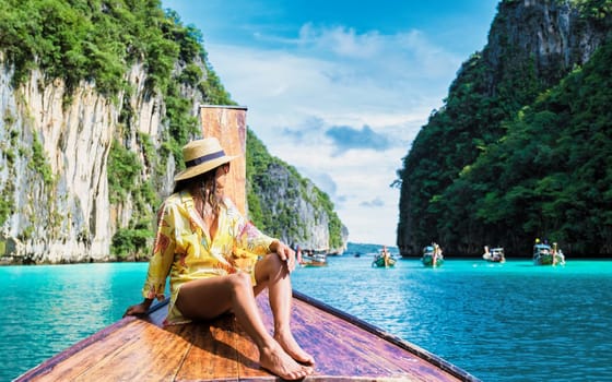Asian women in front of a longtail boat at Kho Phi Phi Thailand, women in front of a boat at Pileh Lagoon with turqouse colored ocean during a trip to Maya Bay