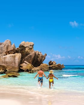 Anse Cocos beach La Digue Island, Seychelles, diverse mixed multiracial multiethnic couple Caucasian men and Asian woman walking at the beach during sunset at a luxury vacation
