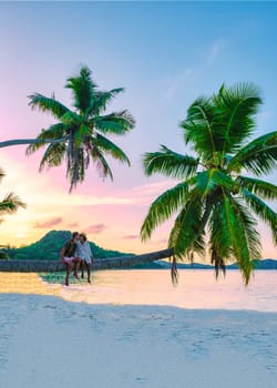 Praslin Seychelles tropical island with white beaches and palm trees, a couple of men and a woman sitting on a palm tree at Anse Volber Seychelles watching the sunset