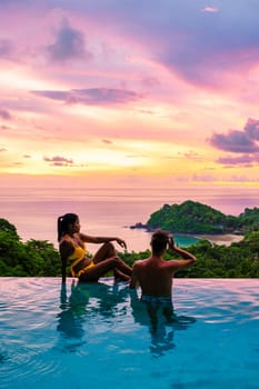 a young couple of men and women at a swimming pool during a vacation on a tropical island. man and woman in an infinity pool during sunset. luxury vacation in Thailand pool of a luxury pool villa