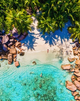 a couple of men and women mid age on vacation at Seychelles visiting the tropical beach of Anse Lazio Praslin Seychelles. Drone view from above at a tropical bay in the Seychelles with palm trees