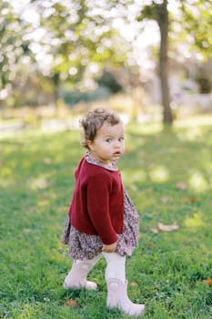 Little girl is standing on the green grass in the garden, looking interestedly to the side. High quality photo