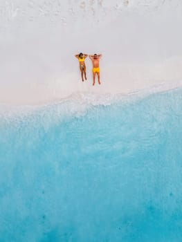 Drone top view of a couple of men and women lying down on the beach of Small Curacao Island, a couple relaxing on the beach of Curacao