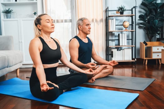 Happy active senior couple in sportswear being doing yoga in meditation posture on exercising mat at home. Healthy senior pensioner lifestyle with peaceful mind and serenity. Clout