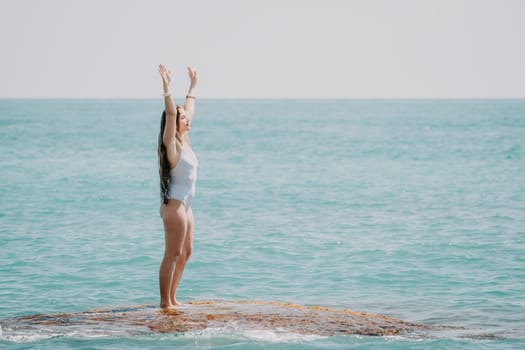 Woman sea yoga. Back view of free calm happy satisfied woman with long hair standing on top rock with yoga position against of sky by the sea. Healthy lifestyle outdoors in nature, fitness concept.