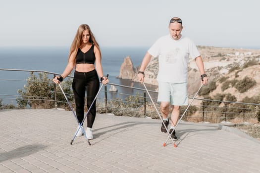 Happy Middle aged couple or friends practicing nordic walking in park near sea. Mature couple with trekking poles walking, practicing Nordic walking outdoors. Aging youthfully and sport concept.