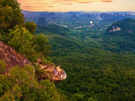 Dragon Crest Mountain Krabi Thailand, a Young couple of travelers sits on a rock that overhangs the abyss, Dragon Crest or Khuan Sai at Khao Ngon Nak Nature Trail in Krabi, Thailand