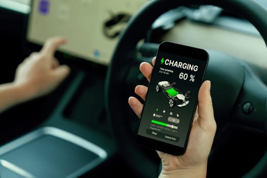 Holiday vacation road trip with environmental-friendly car concept. Eco-conscious woman on driver seat checking EV car's battery status display on smartphone during car travel. Perpetual