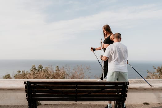 Happy Middle aged couple or friends practicing nordic walking in park near sea. Mature couple with trekking poles walking, practicing Nordic walking outdoors. Aging youthfully and sport concept.