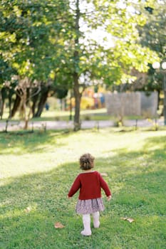 Little girl walks on the green grass in the garden. Back view. High quality photo