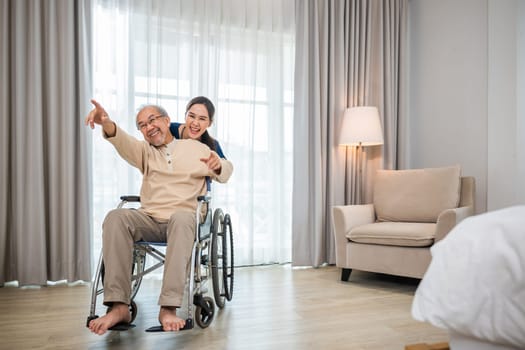 Happy curator person doctor pushing and walk elderly patient freedom raising arm at hospital, Asian senior retired old man sitting on wheelchair having fun with young woman nurse, disabled sanatorium