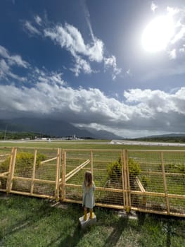 Little girl stands near a metal fence and looks at the airport runways. High quality photo