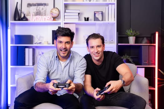 Winner and loser players of buddy friend gamers playing video game on TV using joysticks in studio room with neon blue light. Comfy living indoor at home place with cheerful fighting winner. Sellable.