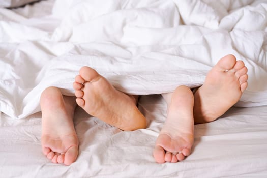 Feet of a couple in bed under the white blanket