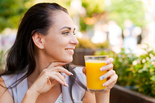 Happy business woman in street cafe drinks natural juice and smiles on sunny day