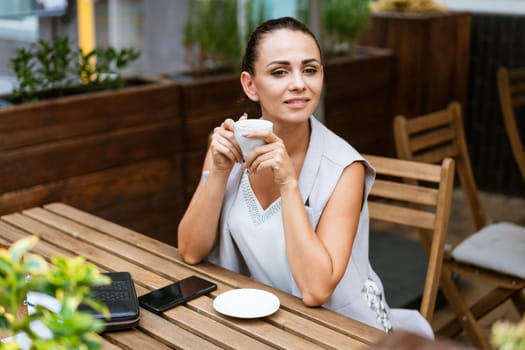Happy smiling business brunette drinking coffee in a street cafe. Coffee break, lifestyle concept. Outdoor portrait
