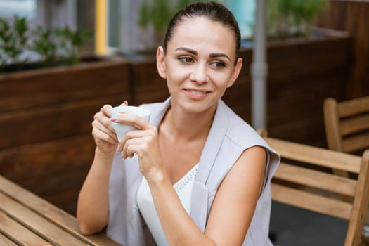 Positive business woman sitting in outdoor cafe drinking coffee
