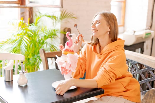 Happy woman eating sweet dessert in form pink flamingo in restaurant, woman sitting in a cafe and enjoying a sweet dessert for lunch, sweet tooth concept