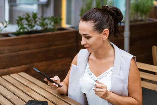 Business woman sitting in street cafe drinking coffee and talking on phone, coffee break concept