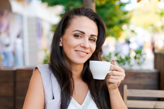 Happy smiling business brunette drinking coffee in a street cafe. Coffee break, lifestyle concept. Outdoor portrait