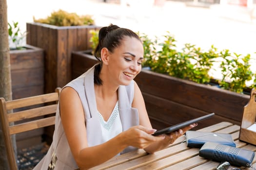 Beautiful businesswoman with smile sitting with touchpad in cozy restaurant while relaxing outside, happy female student working on a digital tablet and relaxing in a cafe after university