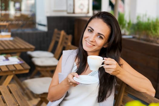 Positive business woman sitting in outdoor cafe drinking coffee