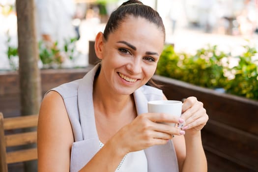 Happy smiling business brunette drinking coffee in a street cafe. Coffee break, lifestyle concept. Outdoor portrait