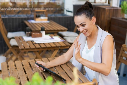 Beautiful businesswoman with smile sitting with touchpad in cozy restaurant while relaxing outside, happy female student working on a digital tablet and relaxing in a cafe after university