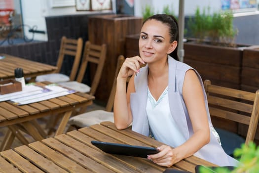 Beautiful businesswoman with smile sitting with touchpad in cozy restaurant while relaxing outside, happy female student working on a digital tablet and relaxing in a cafe after university