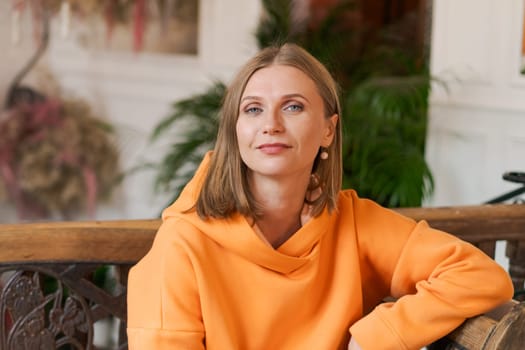 Cute woman in cafe. Portrait beautiful woman, alone at table in cafe. Concept waiting for an order. In a bright orange sweatshirt