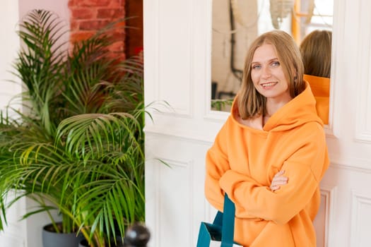 Portrait happy woman in cafe. Wearing a bright orange sweatshirt