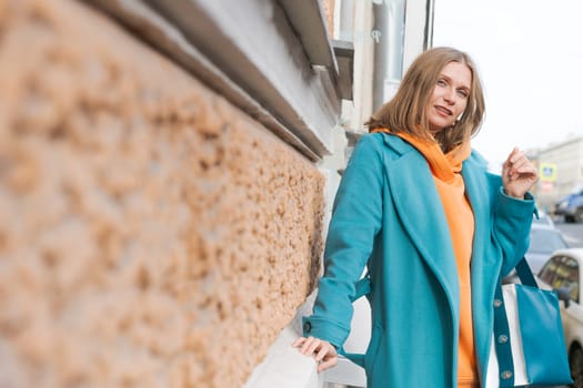 Woman walking through city near canal dressed in bright clothes orange hoodie and blue coat, smiling contentedly, lifestyle concept