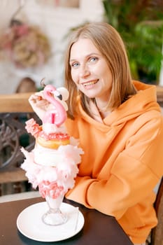 Happy woman eating sweet dessert in form pink flamingo in restaurant, woman sitting in a cafe and enjoying a sweet dessert for lunch, sweet tooth concept