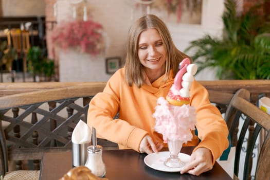 Happy woman eating sweet dessert in form pink flamingo in restaurant, woman sitting in a cafe and enjoying a sweet dessert for lunch, sweet tooth concept