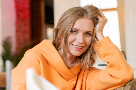 Portrait happy woman in cafe. Wearing a bright orange sweatshirt