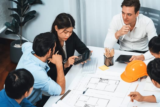 Diverse group of civil engineer and client working together on architectural project, reviewing construction plan and building blueprint at meeting table. Prudent