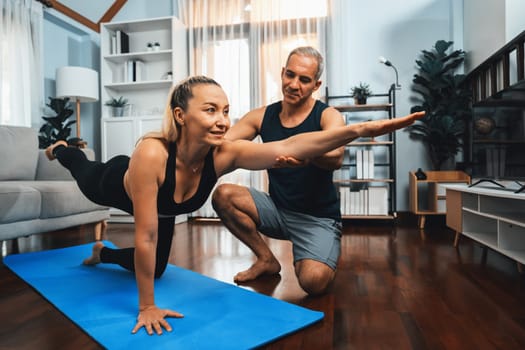 Happy active senior couple in sportswear being supportive and assist on yoga posture together at home. Healthy senior man and woman lifestyle with yoga exercise. Clout