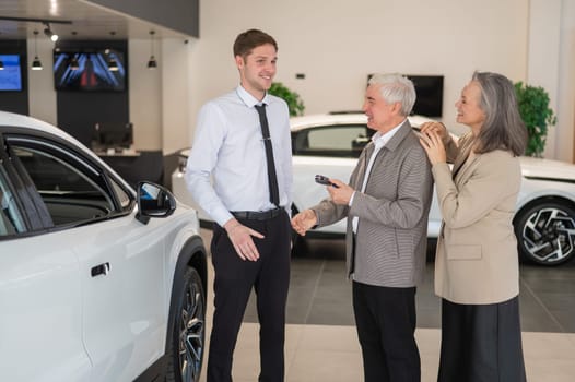 A salesman hands over the keys to a new car to an elderly Caucasian couple