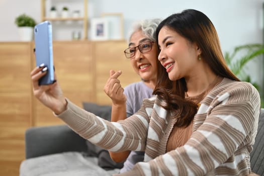 Pretty young Asian lady and mature mother taking selfie on smartphone together.