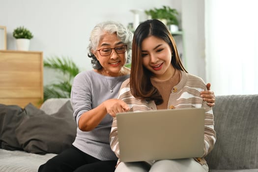 Happy mature mother and adult daughter using laptop surfing internet or shopping via internet.