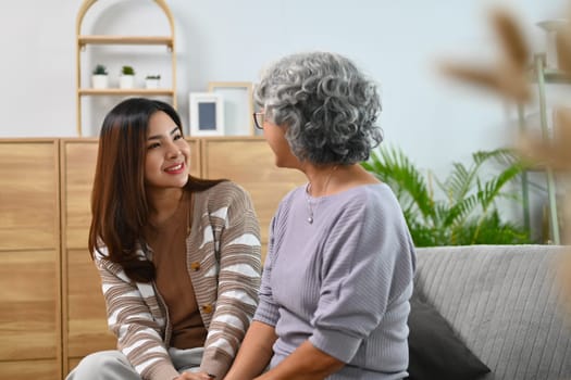 Adult daughter and senior mother having fun enjoying talk while relaxing on couch at home.