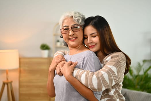 Young adult daughter hugging senior mother while expressing love and enjoying tender moment together.