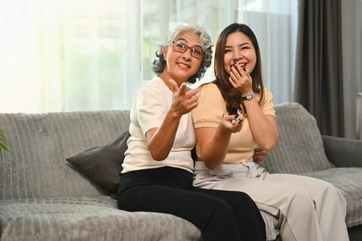 Cheerful senior mother and her daughter sitting on sofa and watching TV.